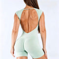 A woman shown from the back wearing a mint green one-piece bodysuit with a large open back and short legs, photographed against a clean white studio background.